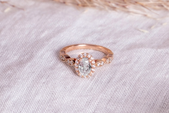 Rose gold engagement ring with oval center diamond on a textured white background.